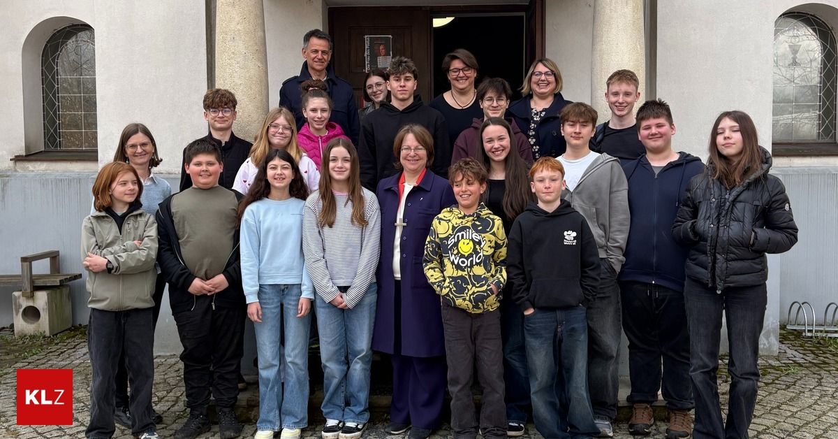 Eine Gruppe von Schülern und Lehrern steht vor einem Gebäude mit einer offenen Tür und einem Schild und posiert für ein Gruppenfoto.