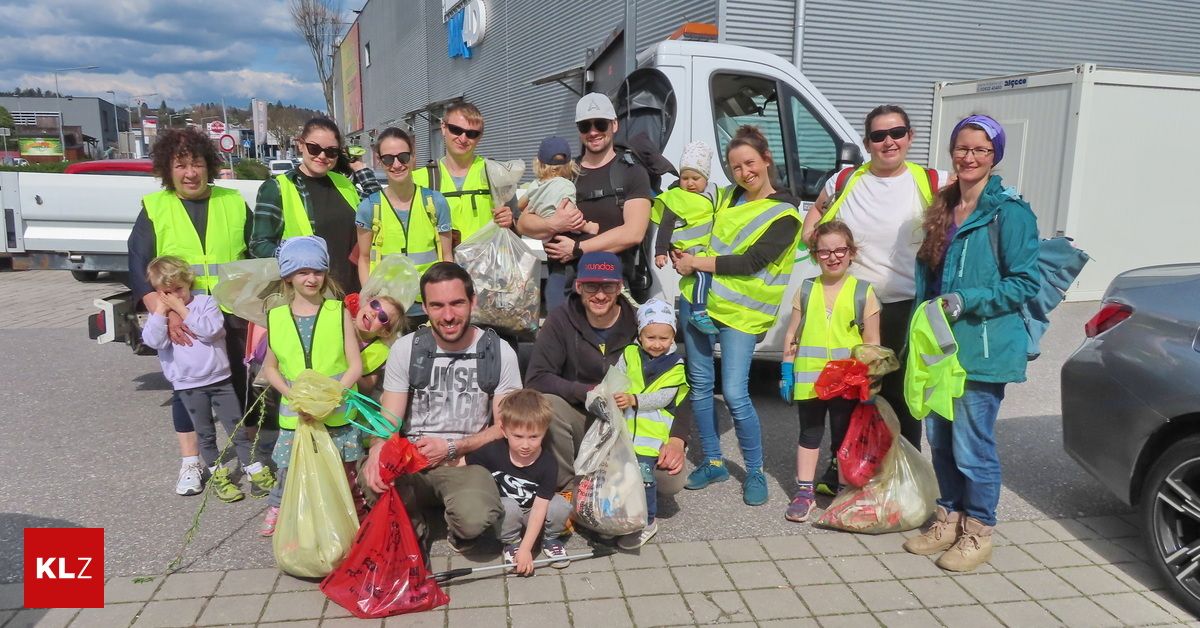 Eine Gruppe von Freiwilligen in Sicherheitswesten mit Säcken voller gesammelter Gegenstände steht vor einem weißen Lieferwagen und lächelt.