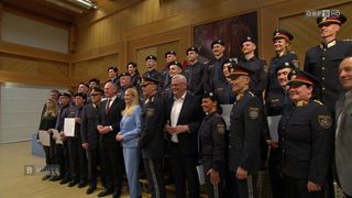 Eine Gruppe von Polizeibeamten steht zusammen mit Offiziellen in formeller Kleidung. Sie alle lächeln und scheinen für ein Foto zu posieren.