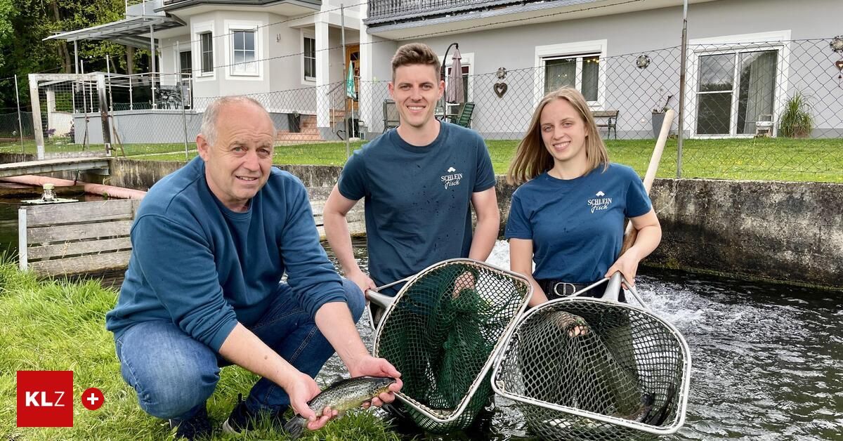 Drei Personen posieren am Bach mit Angelkörben, mit einem Haus und Zaun im Hintergrund.