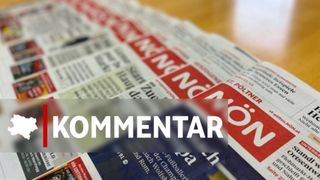 Ein Stapel Zeitungen auf einem Tisch mit dem Wort 'kommentar' in weißer Schrift in der Mitte.