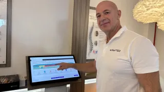Ein Mann in einem weißen Poloshirt mit SchlafTEQ Schriftzug steht vor einem Monitor, der ein Diagramm anzeigt.