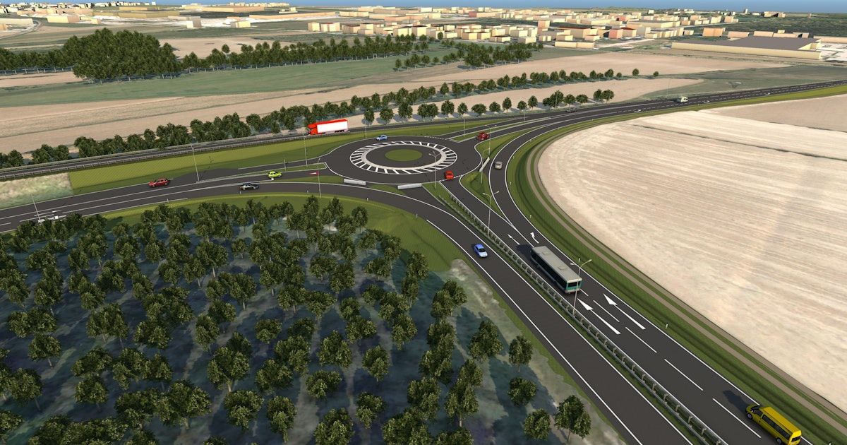 Luftaufnahme einer vielbefahrenen Straße mit mehreren Spuren, Fahrzeugen, einem Kreisverkehr, Bäumen und einer Stadtsilhouette in der Ferne.