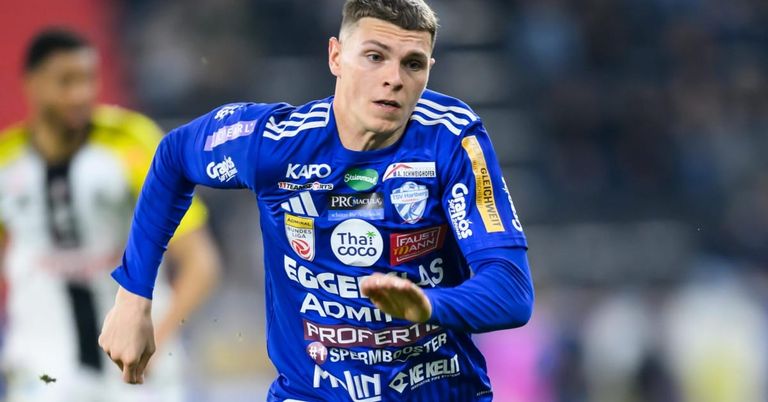 Ein Fußballspieler läuft auf dem Feld in einem blauen Trikot mit mehreren Werbungen. Sein Gesichtsausdruck ist konzentriert.