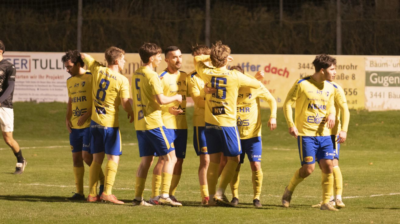 Fußballspieler feiern ein Tor auf dem Feld. Sie tragen gelbe Trikots mit Nummern auf dem Rücken.