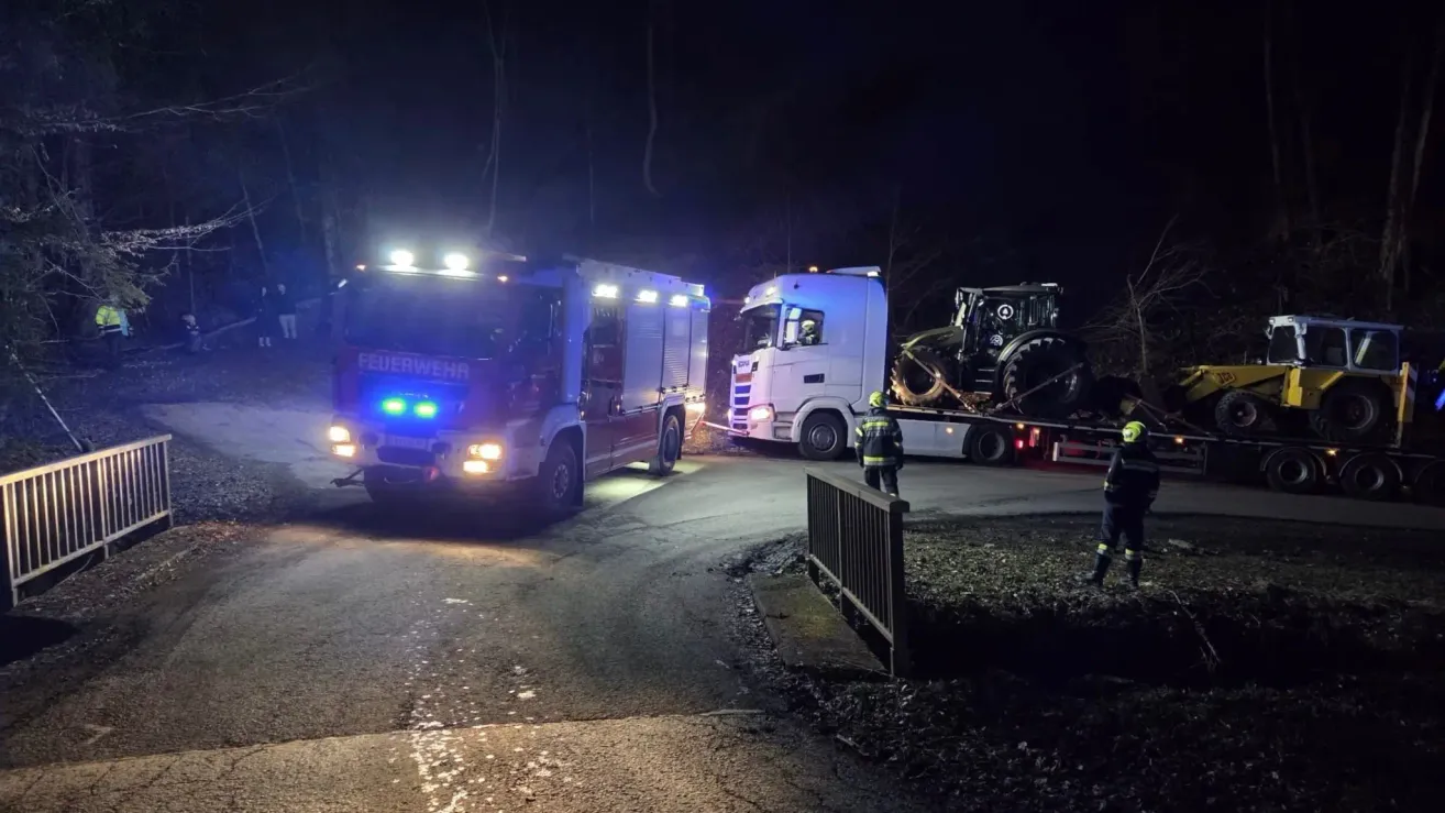 Feuerwehrleute und ein Traktor stehen nachts am Straßenrand. Der Feuerwehrwagen hat blinkende Lichter.