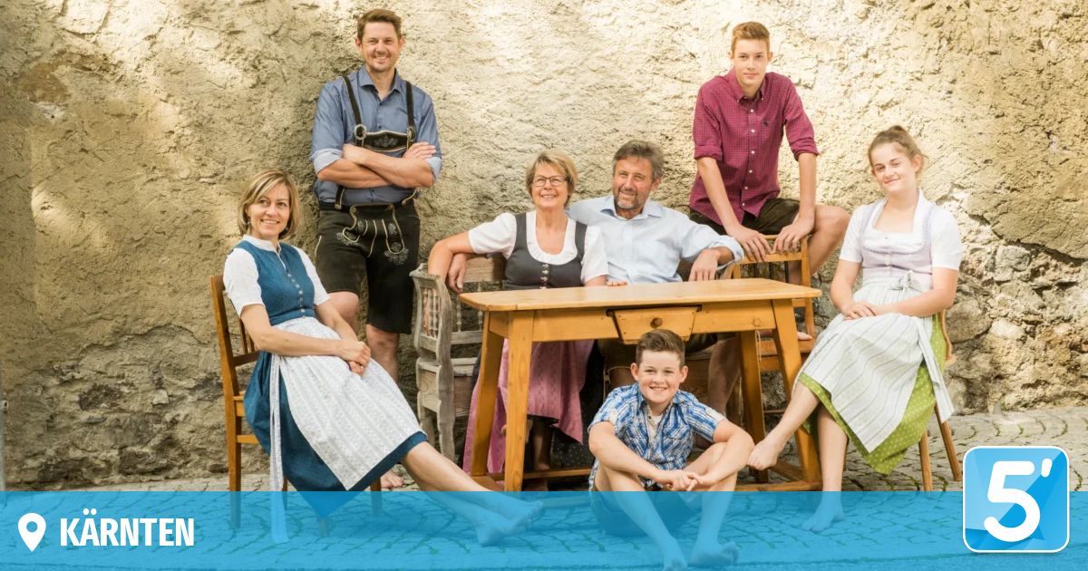 Eine Familie von sieben Personen, die lächelnd und in traditioneller Kleidung für ein Foto posiert, wobei zwei am Tisch sitzen und fünf stehend dahinter.