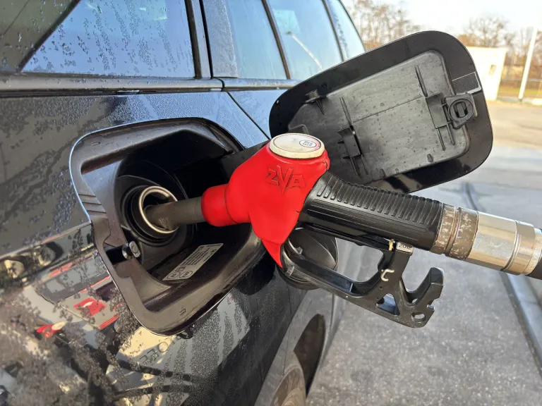 Ein roter Zapfhahn füllt einen schwarzen Wagen mit Benzin. Das Auto hat einen Aufkleber in der Tankklappe.