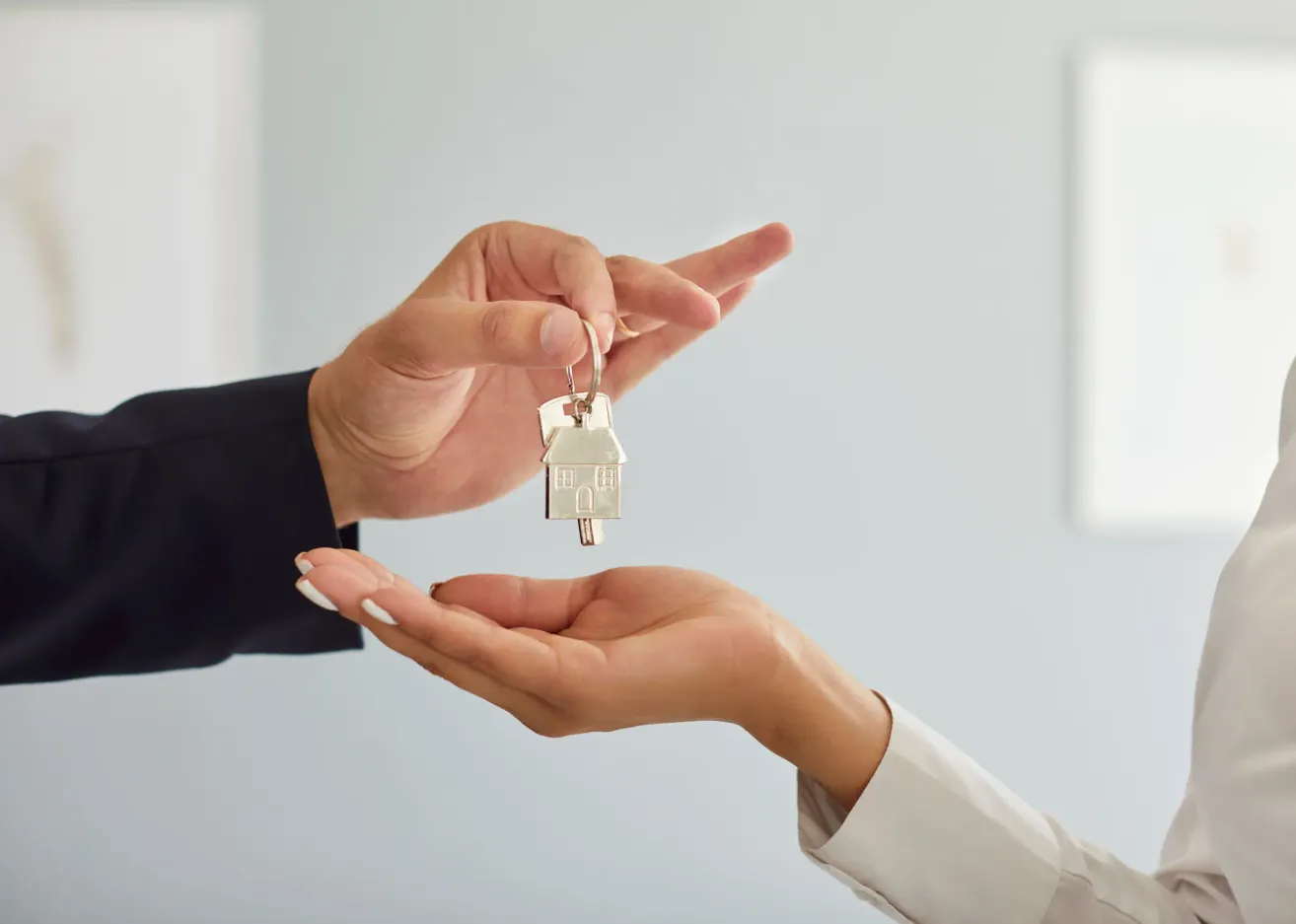 Zwei Hände halten einen Hausschlüssel. Eine Hand gehört einer Person in formeller Kleidung, die andere einer Person im weißen Hemd.
