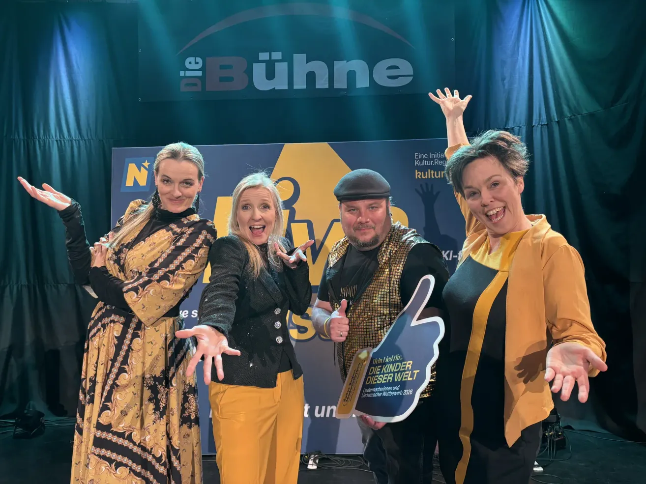 Eine Gruppe von Menschen lächelt und posiert für ein Foto auf der Bühne mit einem Banner hinter ihnen.