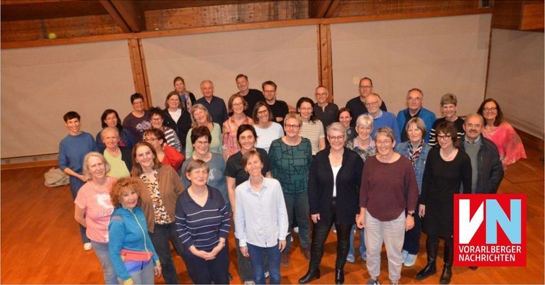 Eine Gruppe von Erwachsenen in formeller Kleidung posiert für ein Foto in einem Raum mit Holzbalken und weißen Wänden.