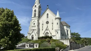 Eine weiße Kirche mit zwei Türmen steht auf einem Hügel, umgeben von Grün und einem klaren blauen Himmel.