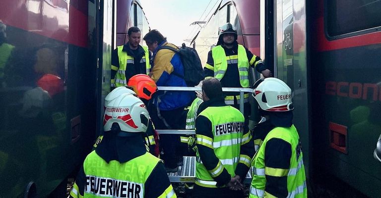 Feuerwehrleute in neongrünen Uniformen und Helmen helfen einem Mann mit Rucksack, möglicherweise auf einem Bahnsteig.