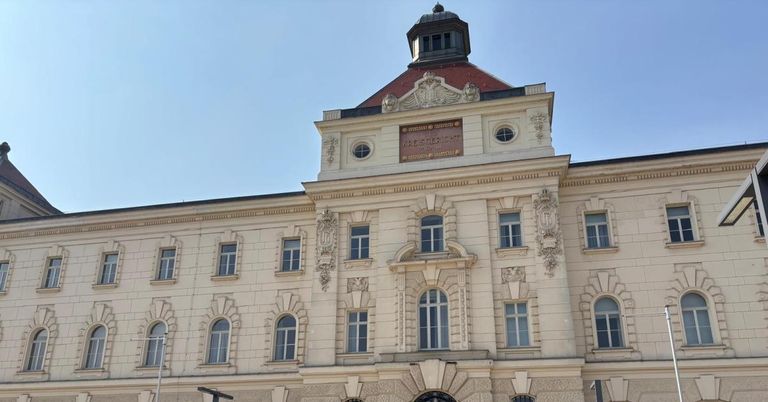 Ein großes weißes Gebäude mit vielen Fenstern und einem Turm mit einem braunen Dach. Ein Schild steht 'Kaiserlicher Hof'.