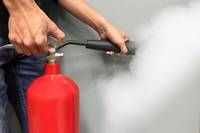 Eine Person hält einen roten Feuerlöscher und setzt weißen Rauch gegen eine graue Wand frei.