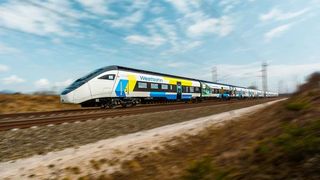 Ein Westbahn-Zug fährt mit unscharfem Hintergrund auf den Gleisen. Der Himmel ist blau mit einigen Wolken.