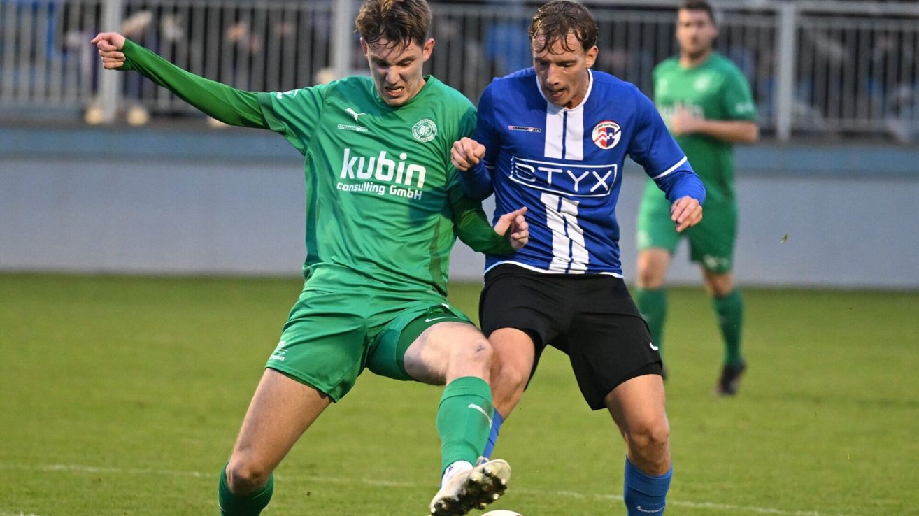 Zwei Fußballspieler kollidieren während eines Spiels. Der Spieler in Grün versucht, den Ball zu schießen.