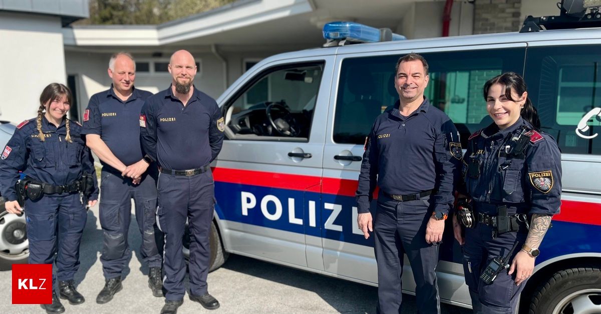 Vier Polizeibeamte stehen vor einem silbernen Polizeiwagen mit 'POLIZEI' an der Seite. Der Wagen hat blaue, rote und weiße Streifen.