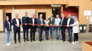 Eine Gruppe von Geschäftsleuten steht vor einem Gebäude mit einem roten Band und feiert eine Eröffnung oder ein Ereignis.