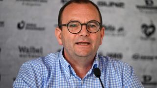 Ein Mann mit Brille sitzt an einem Schreibtisch, schaut in die Kamera und spricht in ein Mikrofon.