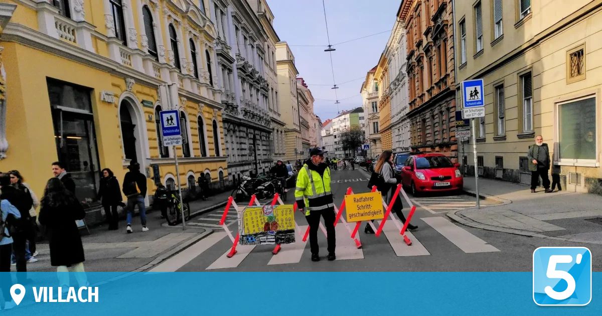 Ein Mann steht auf einem Zebrastreifen in einer Stadt, mit Verkehrszeichen und vorbeigehenden Menschen. Gebäude mit Schildern befinden sich auf beiden Seiten der Straße.
