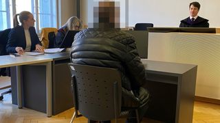 Eine Person sitzt in einem Konferenzraum auf einem Stuhl und sieht einer Frau mit Brille gegenüber. Beide haben Laptops auf ihren Schreibtischen. Eine weitere Person ist hinter der Frau zu sehen.