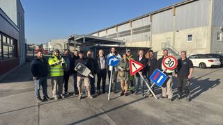 Eine Gruppe von Personen steht vor einem Gebäude und hält jeweils ein Verkehrsschild, einschließlich eines Geschwindigkeitsbegrenzungsschildes.