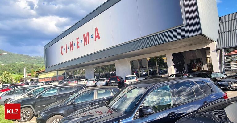 Kino CinemaX mit vielen parkenden Autos davor. Der Himmel ist teilweise bewölkt.
