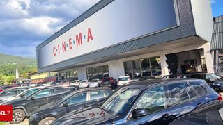 Kino CinemaX mit vielen parkenden Autos davor. Der Himmel ist teilweise bewölkt.