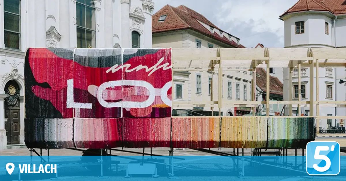 Eine lebendige Straßenkunstinstallation vor einem historischen Gebäude mit einem großen Schild mit dem Wort 'LGO' und einem bunten Regenbogenmuster.