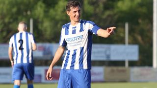 Ein Fußballspieler in einem blau-weiß gestreiften Trikot mit Franye drauf zeigt auf. Er lächelt und spielt auf einem Feld.