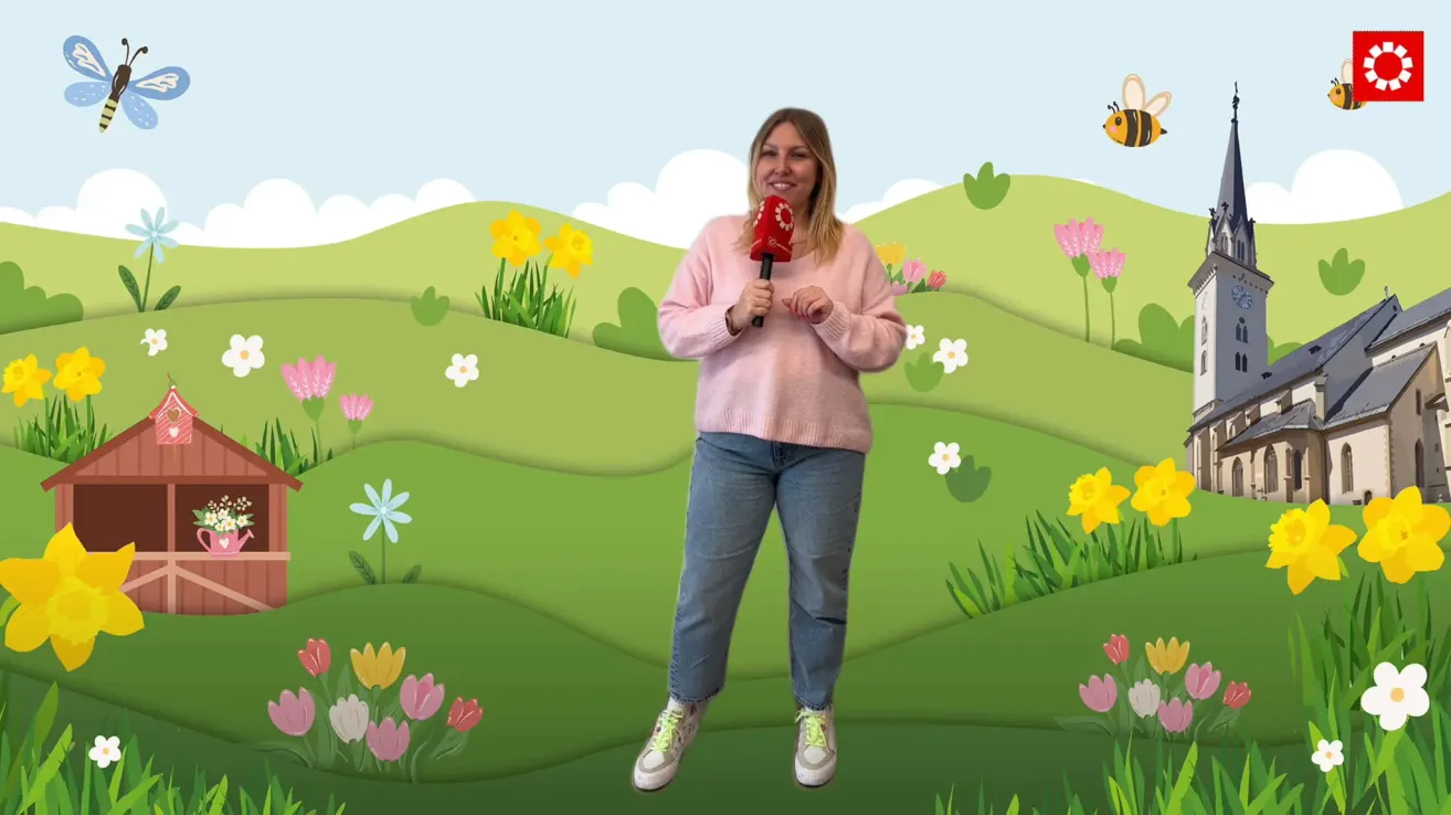 Eine Frau in einem rosa Pullover und blauer Jeans steht in einem Blumenfeld und hält ein rotes Mikrofon.