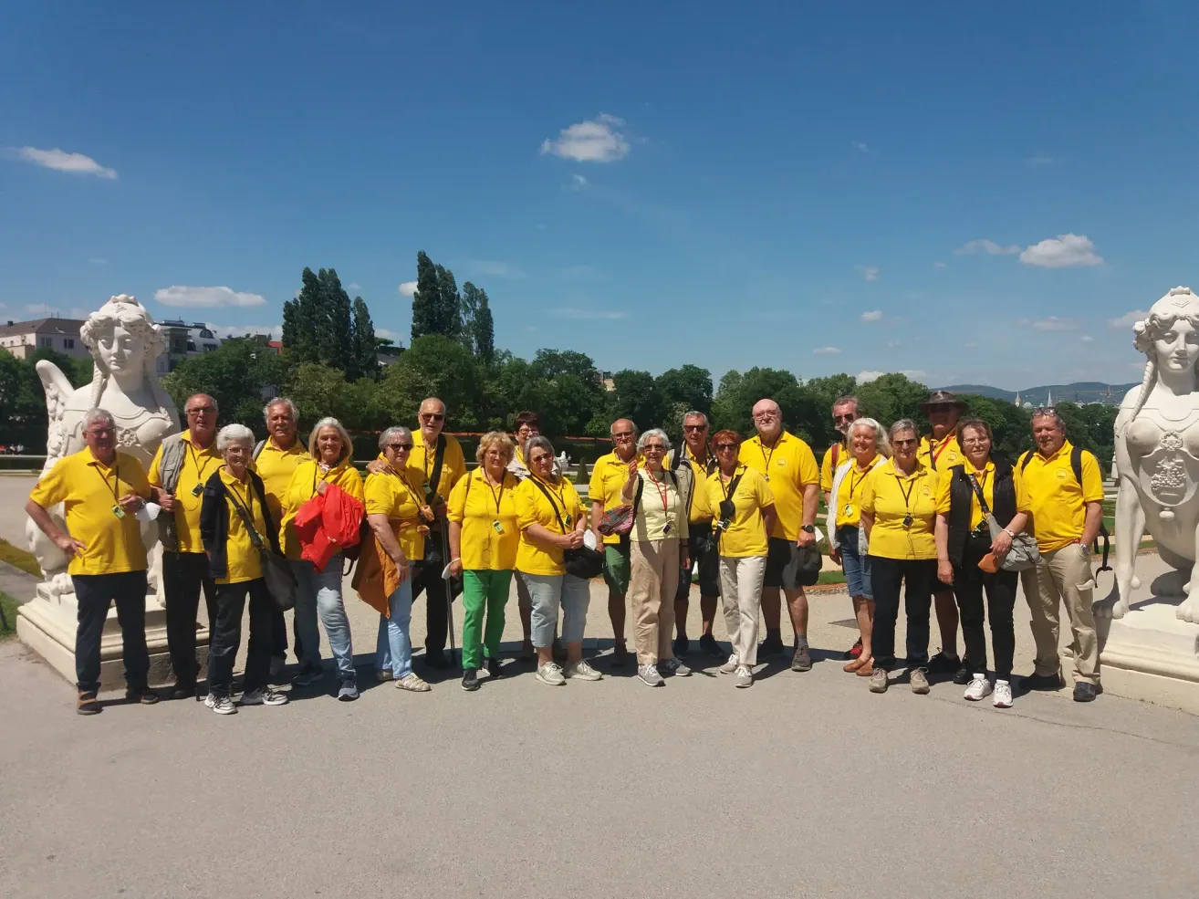 Eine Gruppe älterer Menschen in gelben T-Shirts steht an einem sonnigen Tag in einem Park. Sie lächeln und posieren für ein Foto.