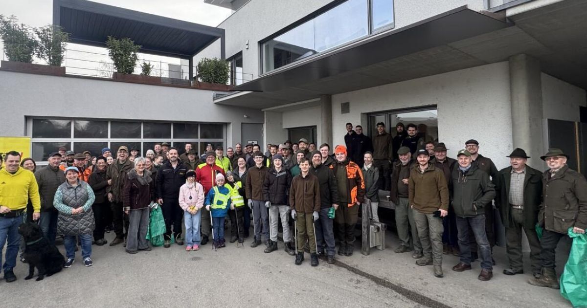 Eine Gruppe von Menschen posiert für ein Foto vor einem Gebäude mit Glaswänden und Pflanzen. Sie tragen Winterkleidung.