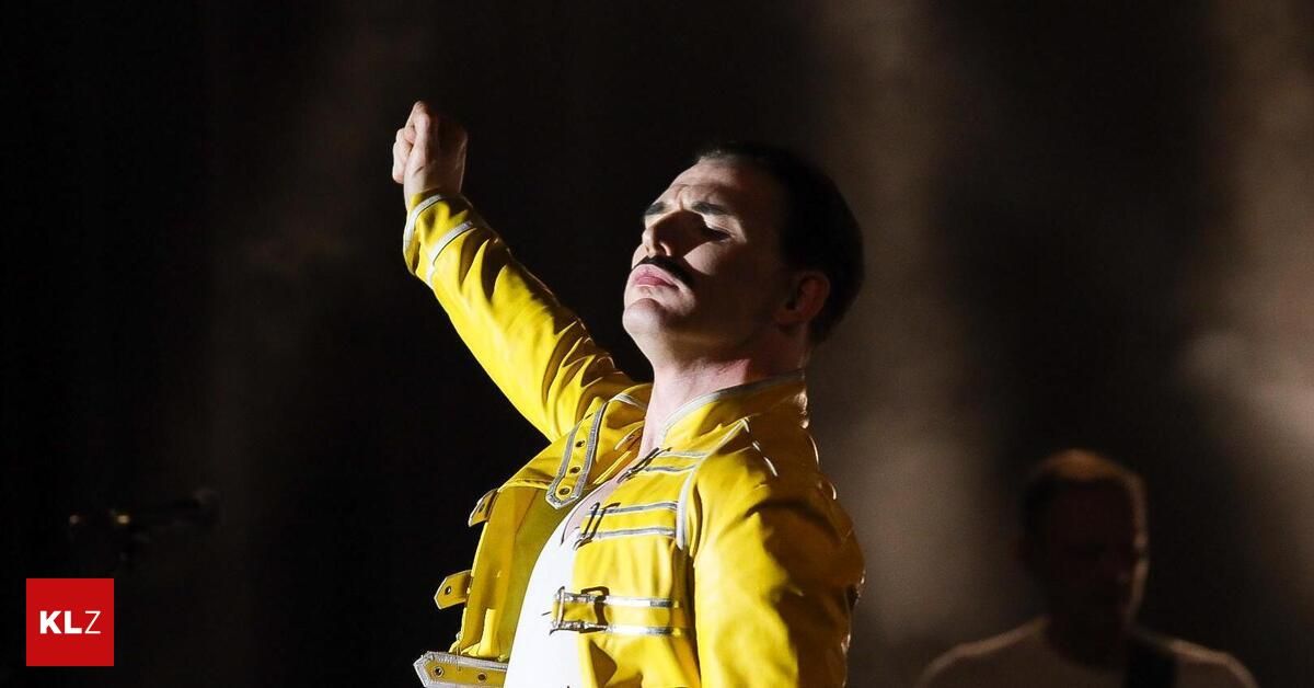 Ein Mann in einem gelben Mantel mit einem weißen Hemd tritt auf der Bühne auf und hebt seine Faust zum Himmel.