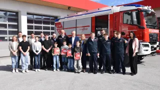 Eine Gruppe von Menschen steht vor einem Feuerwehrauto. Einige halten Urkunden und andere tragen Uniformen.