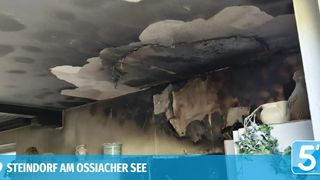 Eine beschädigte Decke mit sichtbaren Wasserschäden und rußigen Flecken, wahrscheinlich von einem Feuer. Gegenstände wie eine Vase und Teller sind darunter sichtbar.