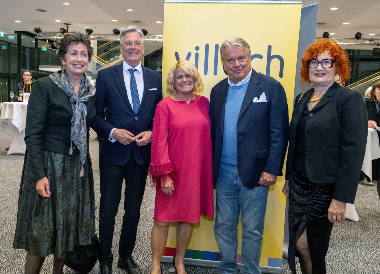 Fünf Personen stehen gemeinsam vor einem gelben Banner. Drei Männer und zwei Frauen, alle lächeln für die Kamera.