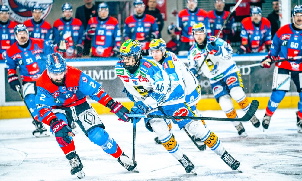 Eishockeyspieler skaten auf dem Eis, zwei Teams in blauen und roten Uniformen, Spieler führen ein körperliches Spiel, Zuschauer im Hintergrund tragen passende Teamfarben.