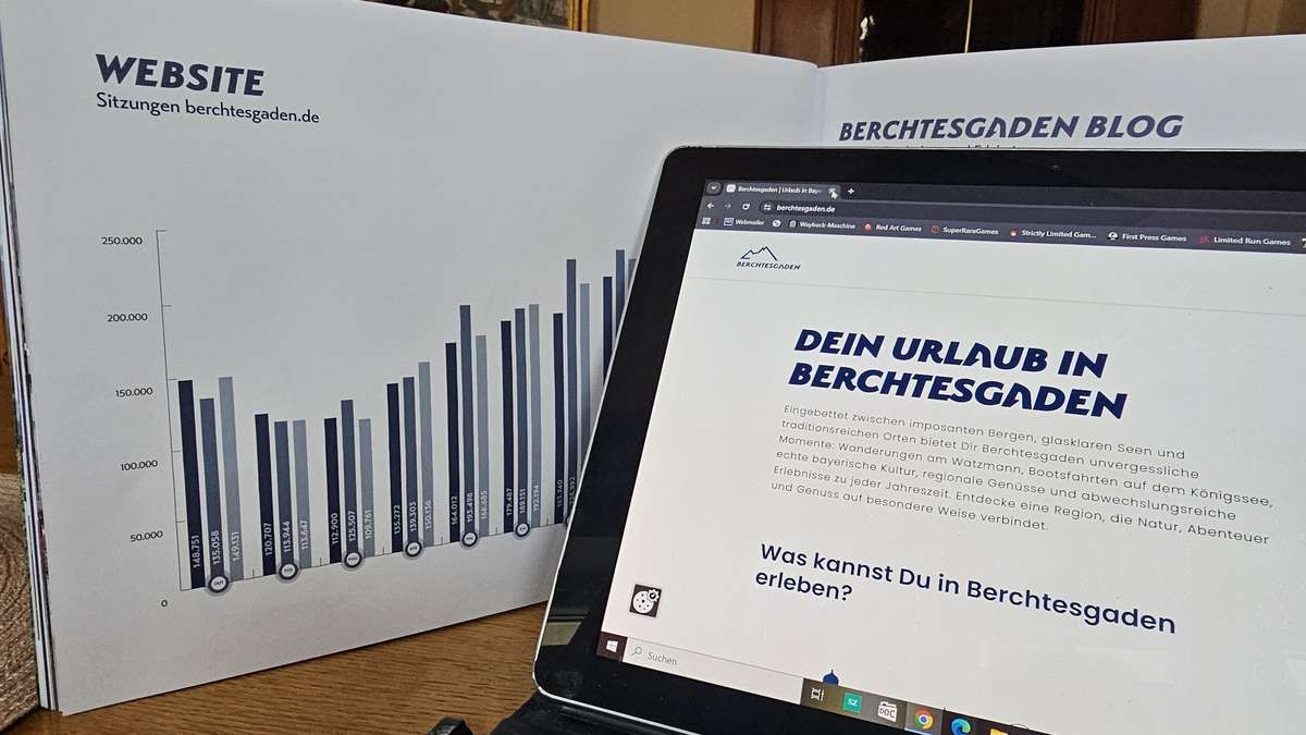 Ein Diagramm der Tourismustrends von Berchtesgaden wird auf einem offenen Prospekt neben einem Laptop angezeigt, der die Website Berchtesgaden.de zeigt.