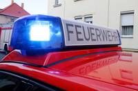 Ein roter Feuerwehrwagen mit blauen Lichtern ist vor einem Gebäude mit Fenstern geparkt. Das Wort 'Feuerwehr' steht auf dem Schild oben auf dem Wagen.