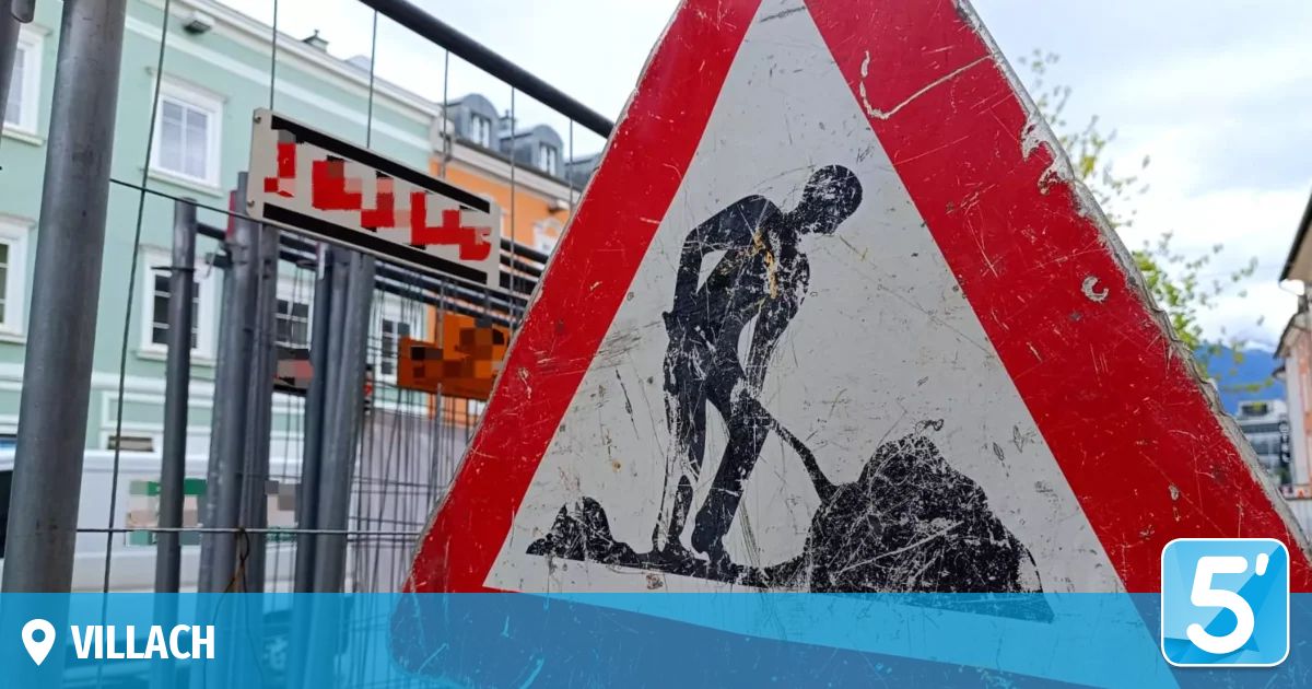 Ein rotes und weißes dreieckiges Schild mit einer graben bauenden Figur. Es befindet sich in der Nähe eines Gebäudes und einer Metallumzäunung.