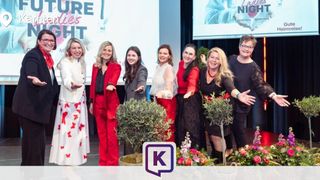 Eine Gruppe von Frauen in Rot und Weiß steht vor einer Bühne und posiert lächelnd für ein Foto.