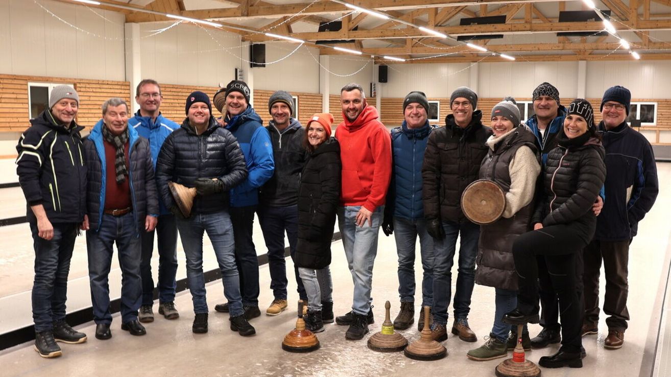 Eine Gruppe von Personen in Winterkleidung posiert für ein Foto in einer Sporthalle und hält Holzbecher in den Händen.
