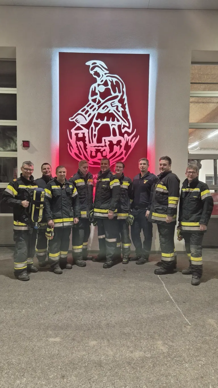 Eine Gruppe von Feuerwehrleuten in Uniform posiert für ein Foto vor einem Feuerwehrschild.