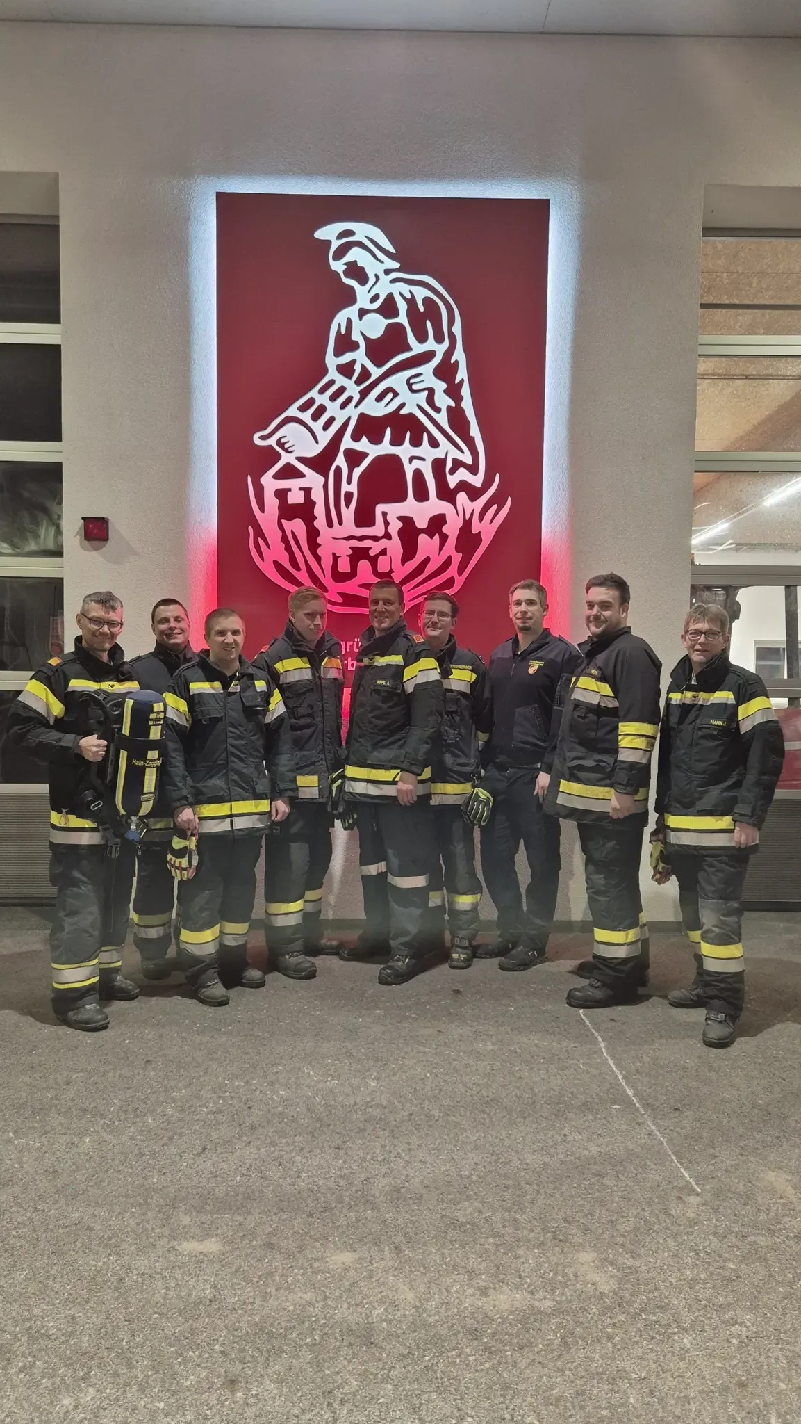 Eine Gruppe von Feuerwehrleuten in Uniform posiert für ein Foto vor einem Feuerwehrschild.
