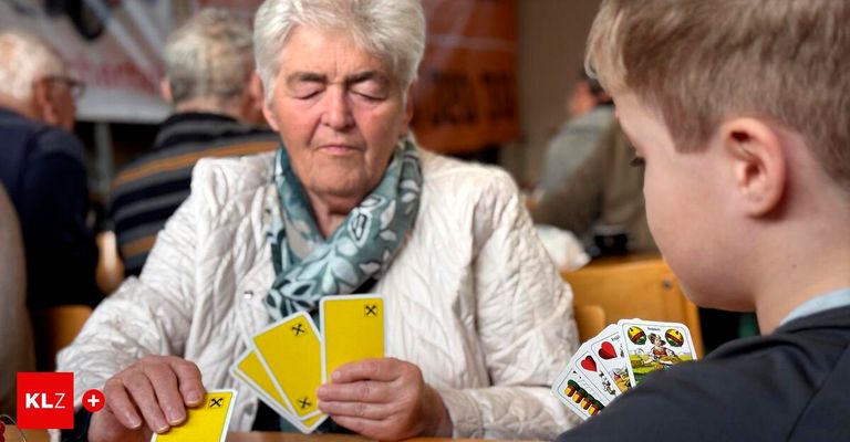 Eine ältere Frau hält gelbe Karten und schaut einen Jungen an, der vor ihr spielt. Hinter ihnen sitzt ein Mann und beobachtet.