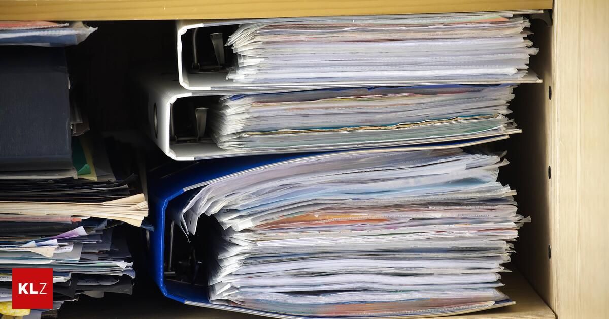 Mehrere Ordner, die aufeinandergestapelt sind, einige mit sichtbarem Papier. Die Ordner sind in verschiedenen Farben und Größen.