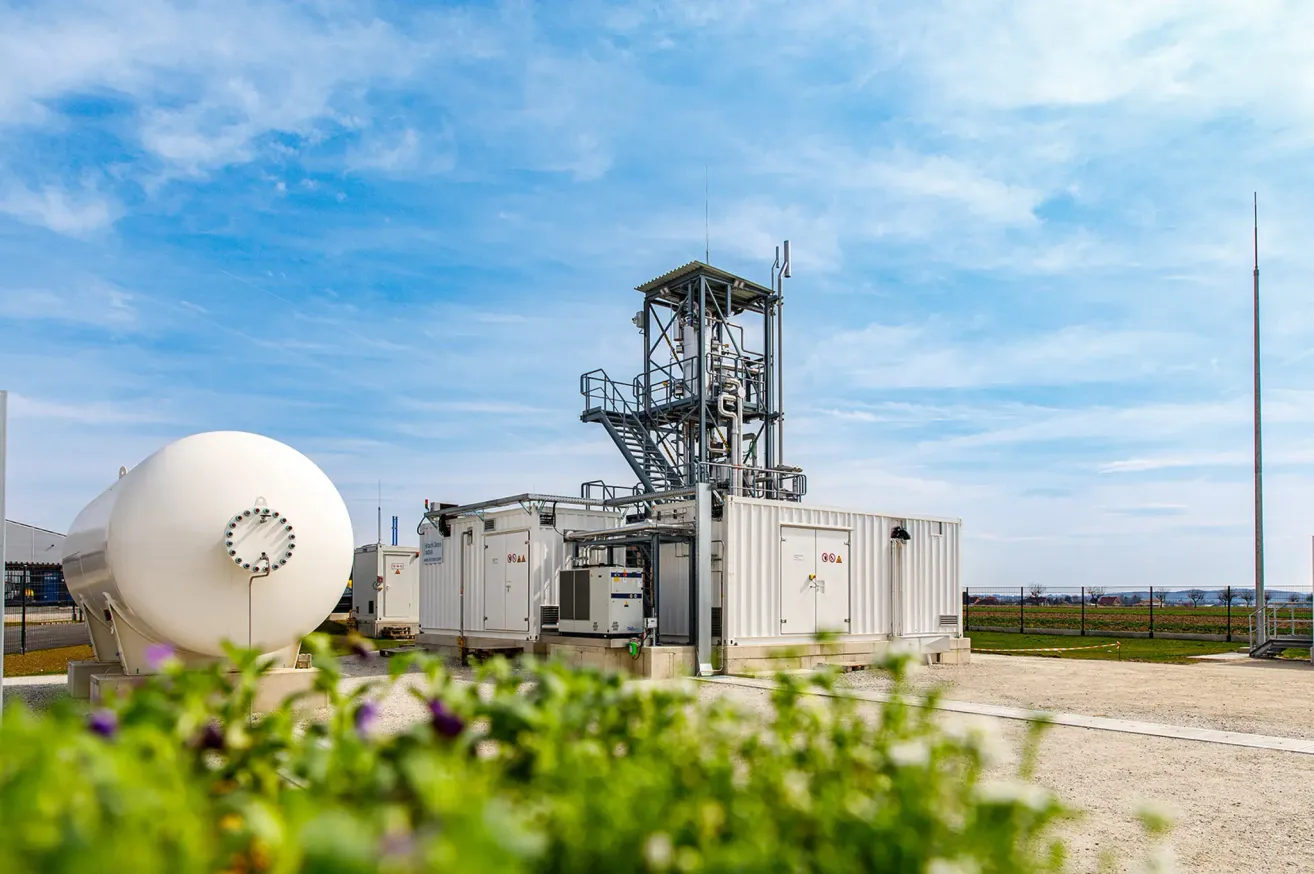 Eine Industrieanlage mit einem großen weißen Lagertank, Metallstrukturen und einem klaren blauen Himmel mit Wolken.