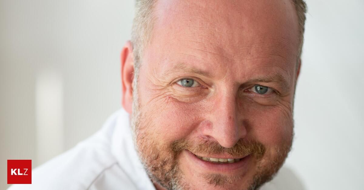 Ein Nahaufnahme des Gesichts eines Mannes mit blauen Augen, einem Bart und einem weißen Hemd. Er lächelt und zeigt die Zähne.